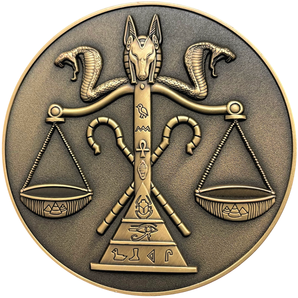 Gold metal coin showing jackal head and cobras on top of scale with Egyptian symbols