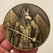 Gold metal coin in hand with Anubis next to pyramids