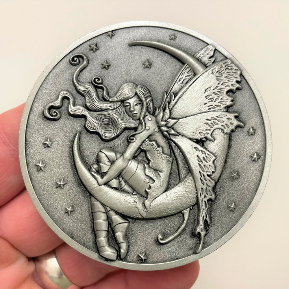 Silver metal coin in hand showing fairy sitting on moon